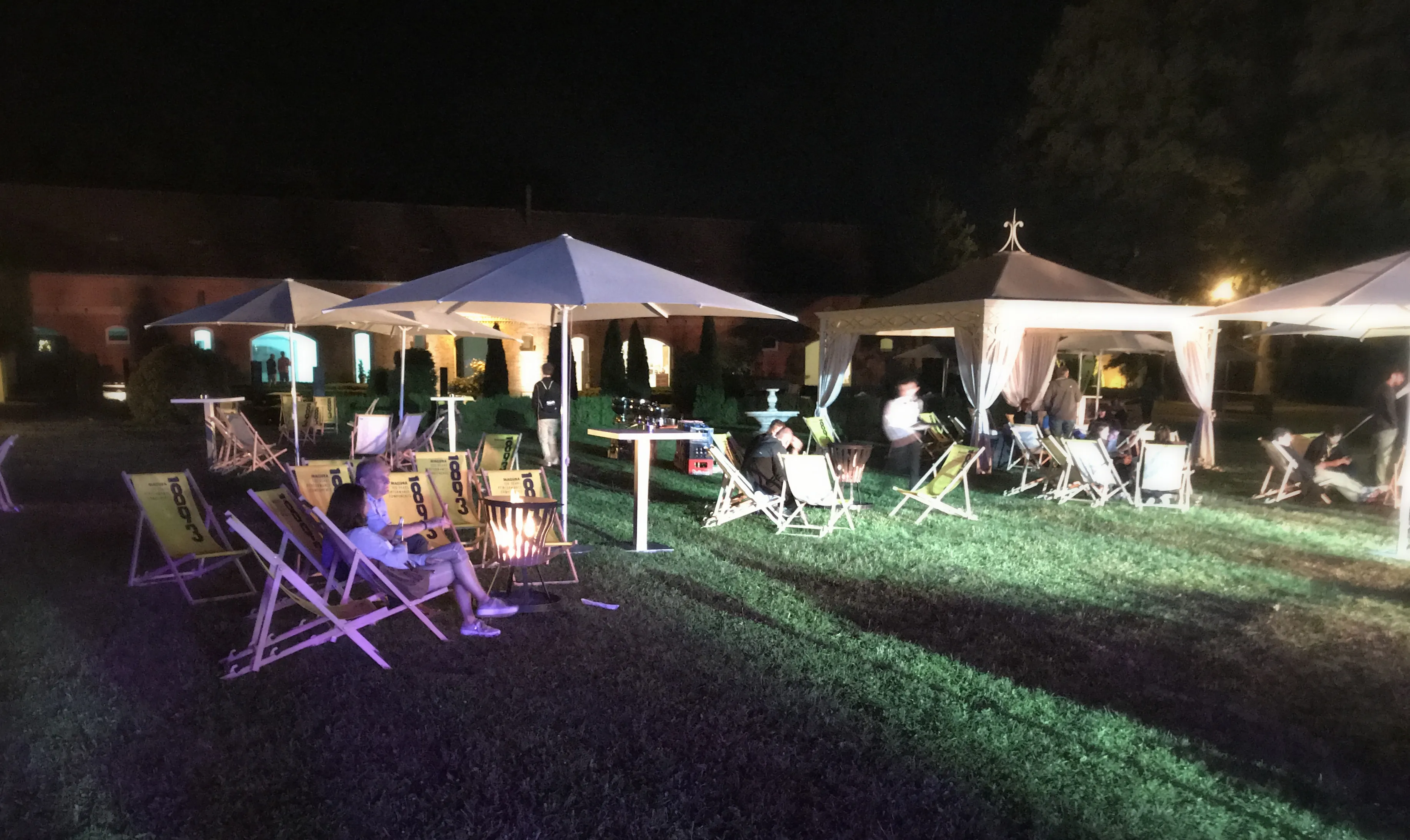 Nächtlicher Garten mit Liegestühlen, Schirmen und warmem Licht