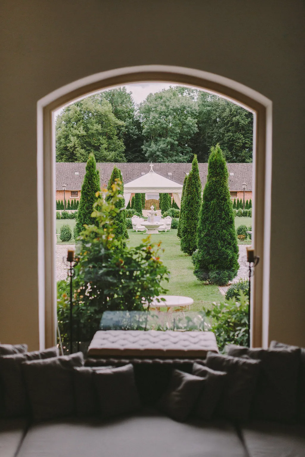 Blick durch ein Fenster in den grünen Garten mit Pavillon und Springbrunnen
